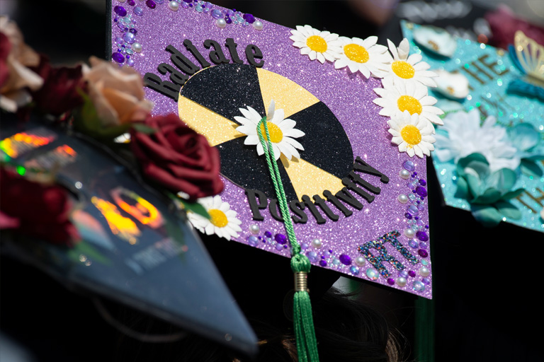 A sparkly purple decorated graduation cap that reads radiate positivity