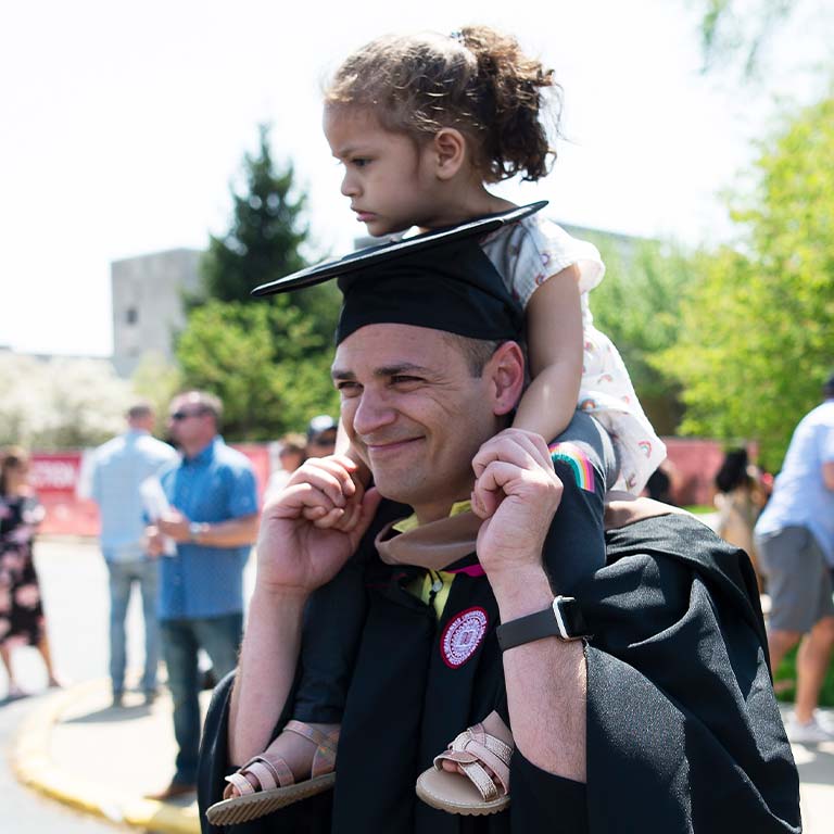 A male graduate carries a little girl on his shoulders after the ceremony